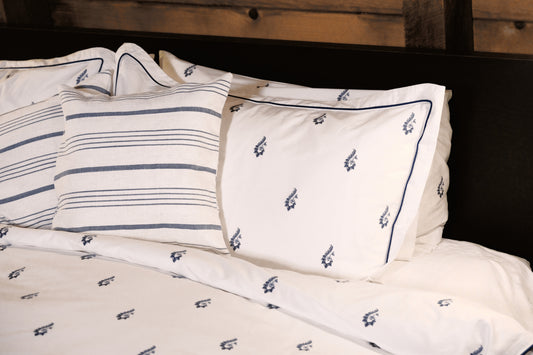 Blue Paisley pillowcases with navy piping beside striped cushions against a dark wood headboard