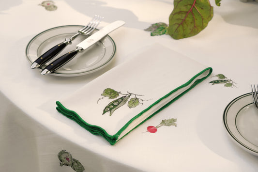 Peapod print napkin with a green overlock hem, folded beside a place setting