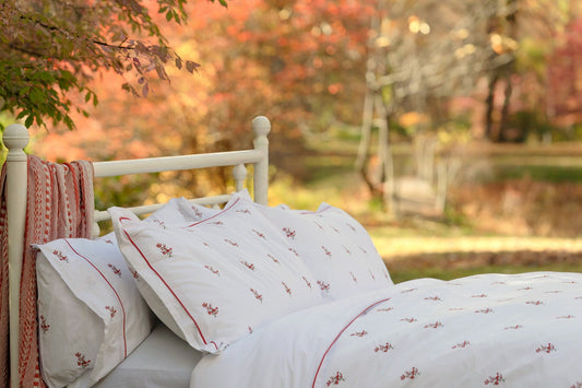 Crimson Meadows bedsheet set on a white bed outdoors in autumn, red floral motifs on white percale