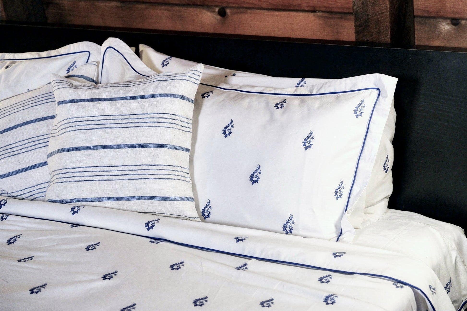 Blue Paisley pillowcases and striped shams against a dark headboard, embroidered navy trim