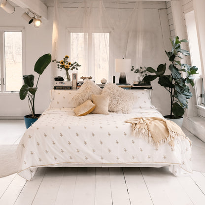 Fields of Gold bedding on a bed in a bright white room with plants and soft cushions