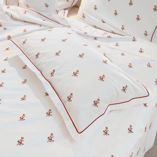 Close-up of a Crimson Meadows pillowcase with red piping and scattered red floral sprays