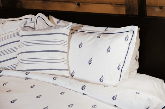 Blue Paisley pillowcases with navy piping beside striped cushions against a dark wood headboard