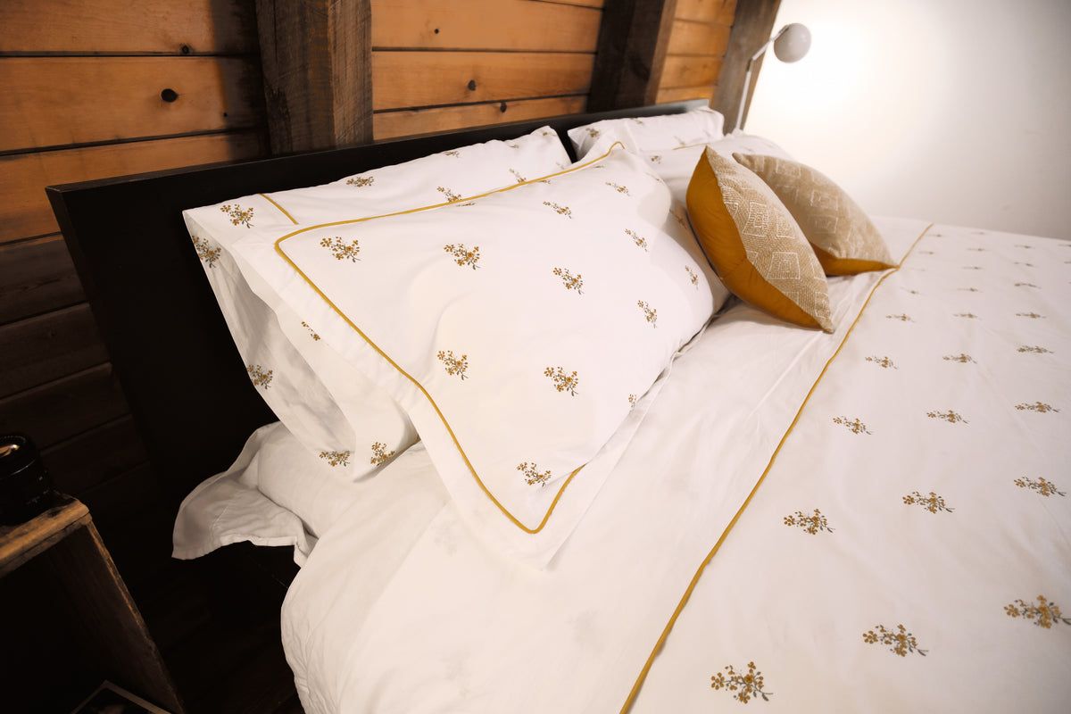 Fields of Gold bedding with mustard piping and golden cushions under a wood-paneled ceiling