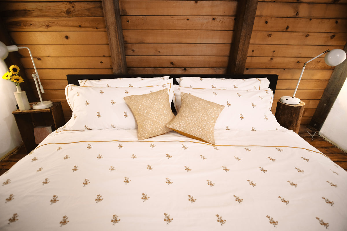 Fields of Gold bedding on a bed in a wood-paneled room with golden cushions and sunflowers