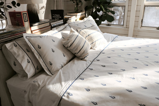 Blue Paisley bedsheet set on a sunlit bed with striped cushions, navy paisley motifs and navy piping on white percale
