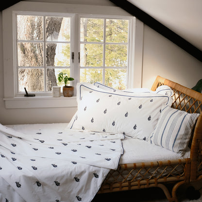 Blue Paisley Embroidered Duvet Set on a rattan daybed by a window, navy embroidered paisleys and navy piping