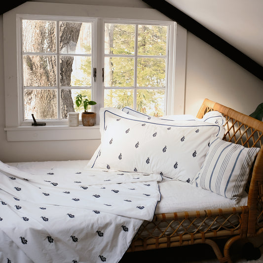 Blue Paisley Embroidered Duvet Set on a rattan daybed by a window, navy embroidered paisleys and navy piping