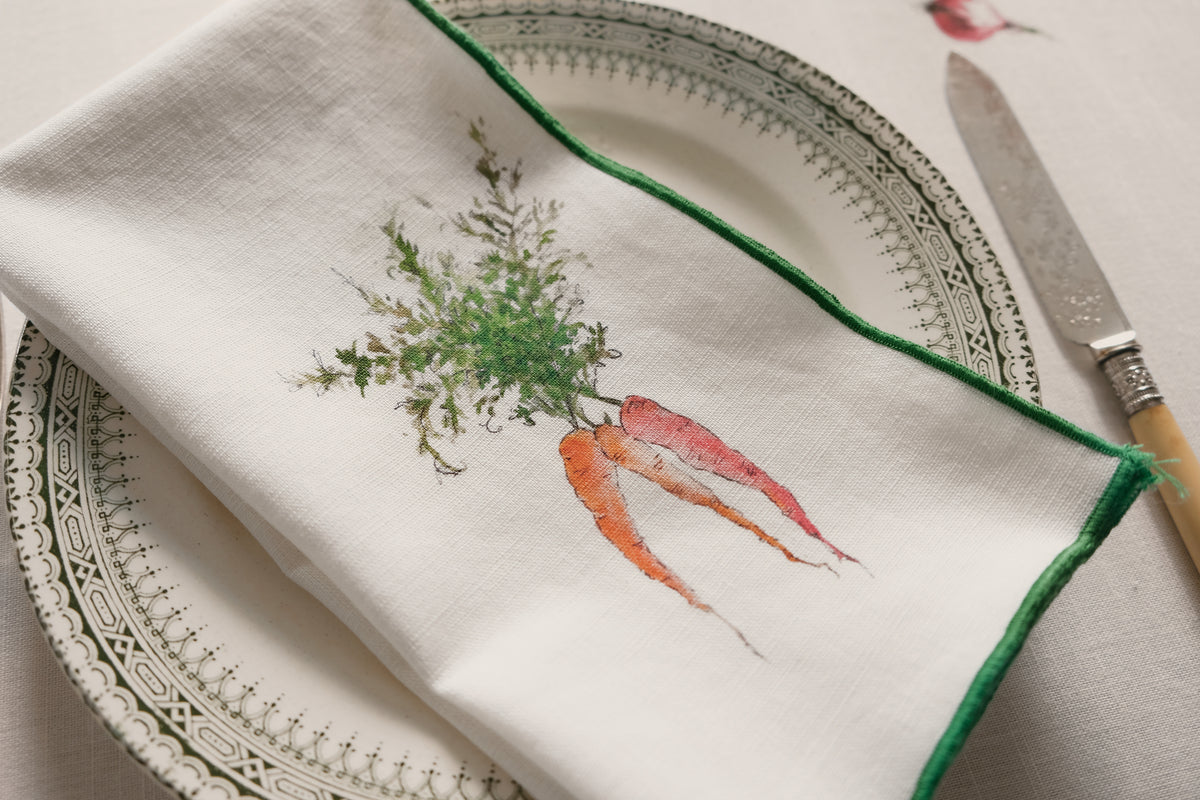 Close-up of the Orange Carrots print napkin with a green overlock hem on a patterned plate