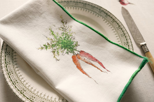 Close-up of the Orange Carrots print napkin with a green overlock hem on a patterned plate