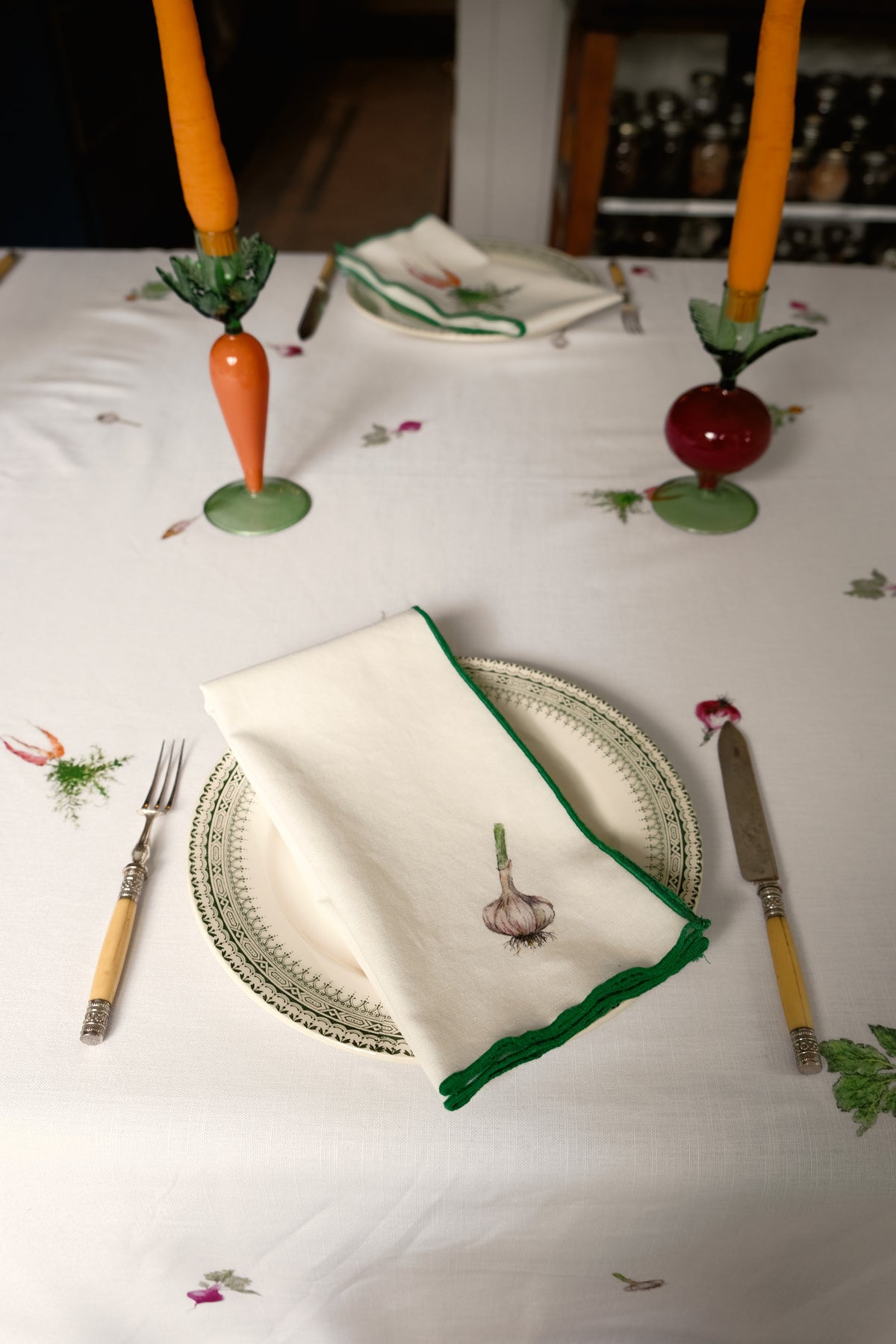 Garlic print napkin with a green overlock hem on a plate, with carrot and beet candlesticks