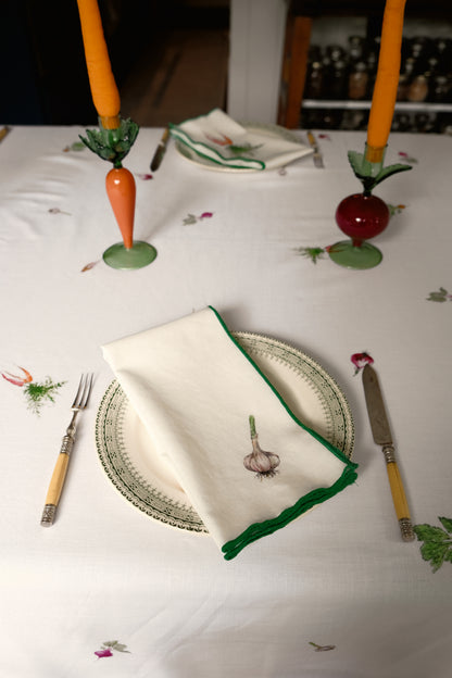 Garlic print napkin with a green overlock hem on a plate, with carrot and beet candlesticks
