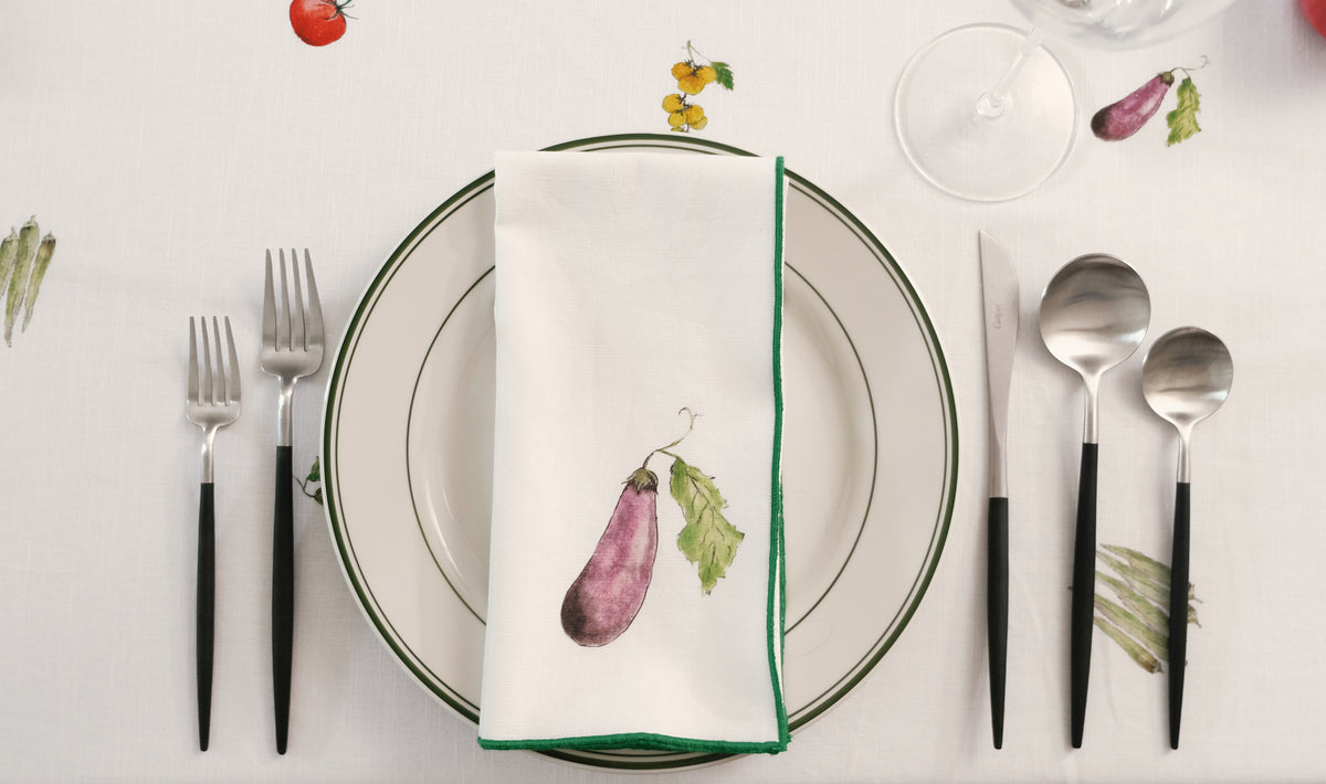 Purple Eggplant print napkin with a green overlock hem on a place setting with black-handled cutlery