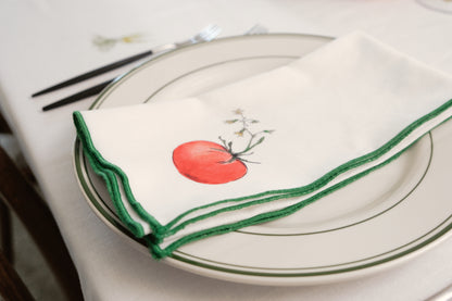 Red Tomato print napkin with a green overlock hem folded on a green-rimmed plate