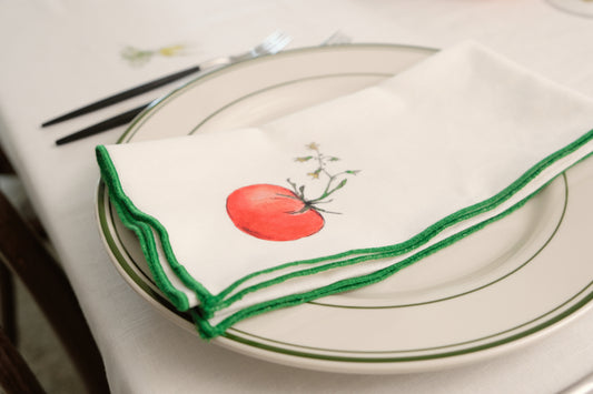 Red Tomato print napkin with a green overlock hem folded on a green-rimmed plate