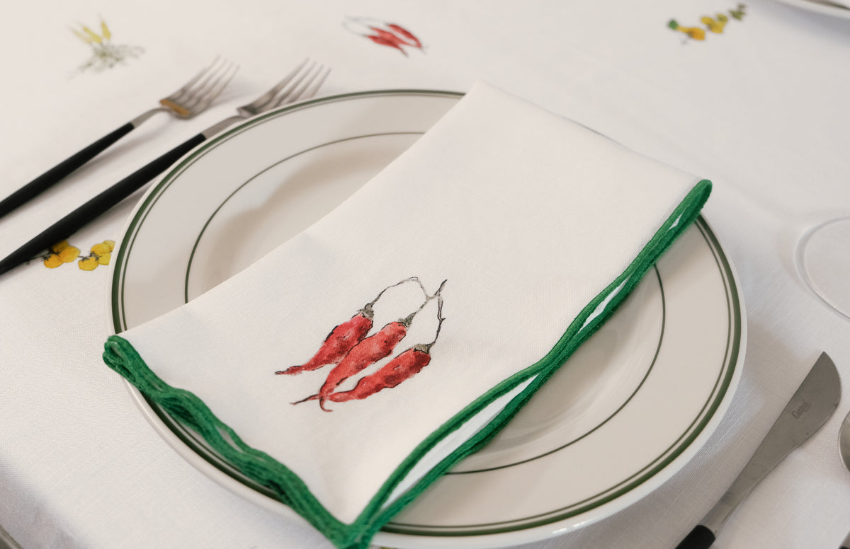 Red Pepper print napkin with a green overlock hem folded across a green-rimmed plate