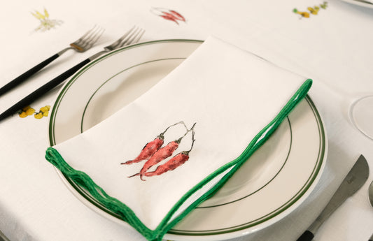Red Pepper print napkin with a green overlock hem folded across a green-rimmed plate