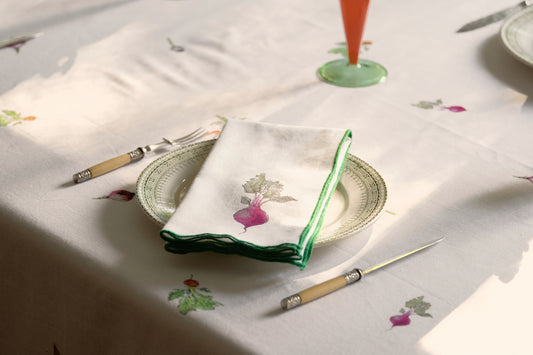 Red Beets print napkin with a green overlock hem folded on a plate on the Root Vegetable Tablecloth