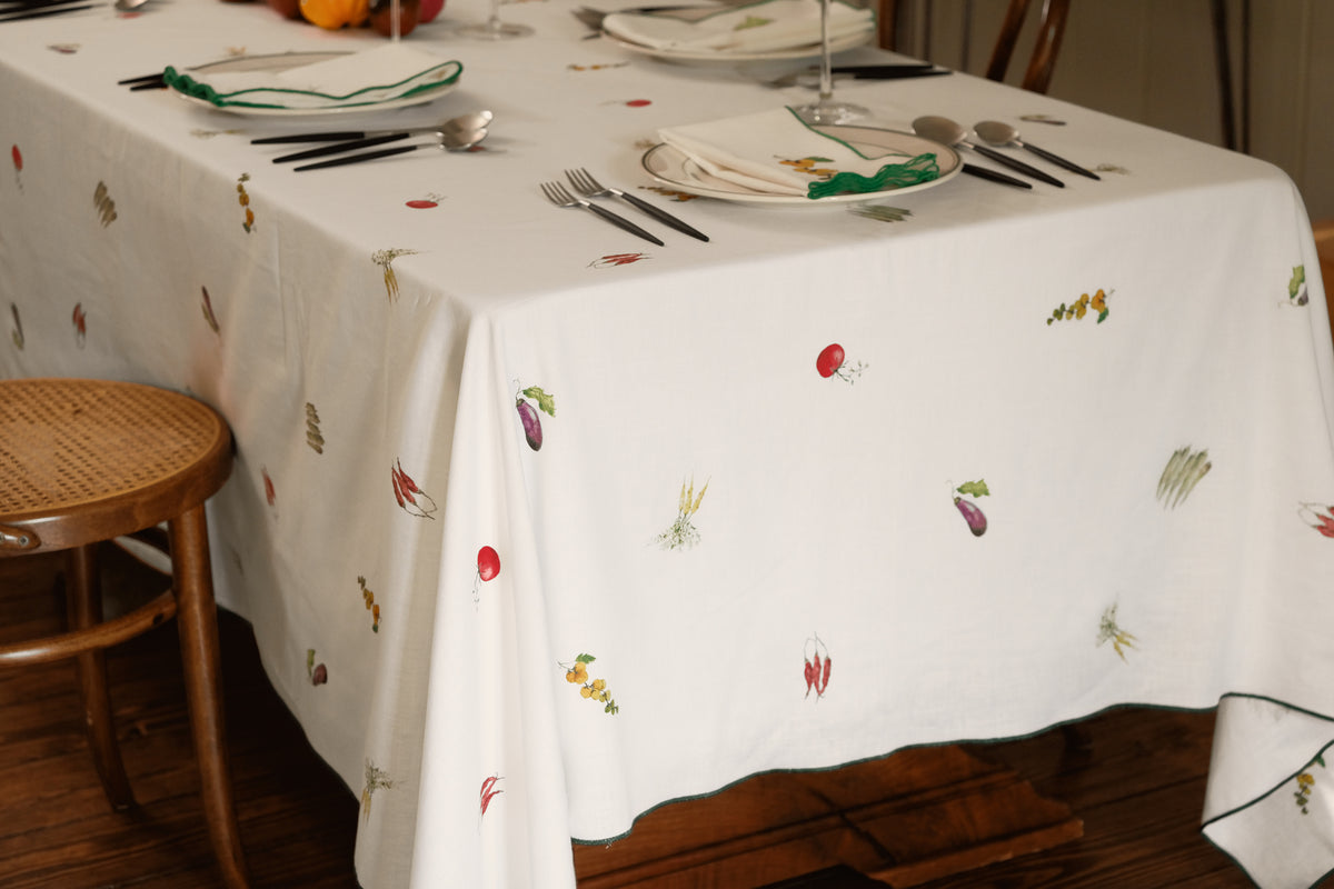 Summer Vegetable Tablecloth draped over a dining table, showing eggplant, tomato and okra motifs and the green hem