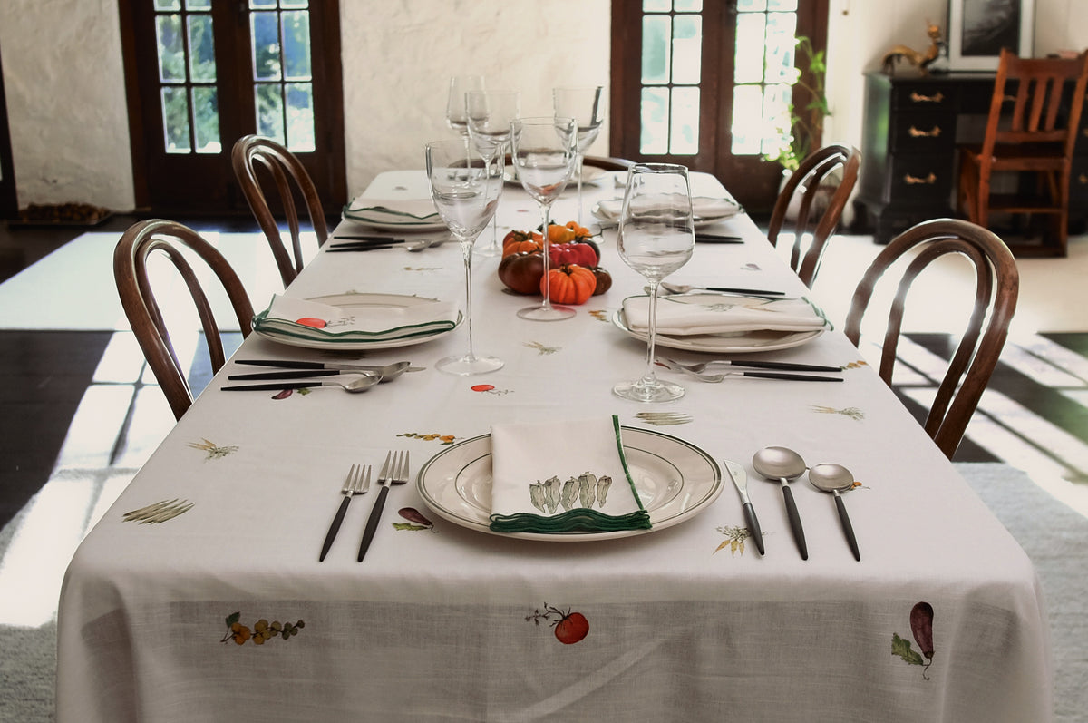 Summer Vegetable Tablecloth on a long dining table set for a dinner party, with glasses, heirloom tomatoes and wooden chairs