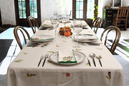 Summer Vegetable Tablecloth on a long dining table set for a dinner party, with glasses, heirloom tomatoes and wooden chairs