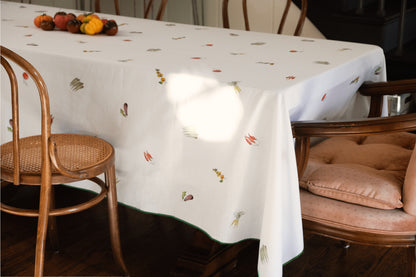 Summer Vegetable Tablecloth on a rectangular table beside bentwood and velvet chairs, with heirloom tomatoes
