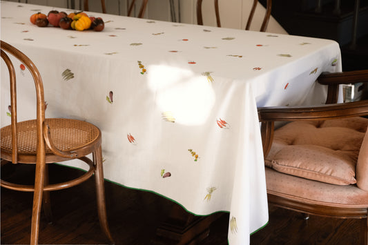 Summer Vegetable Tablecloth on a rectangular table beside bentwood and velvet chairs, with heirloom tomatoes