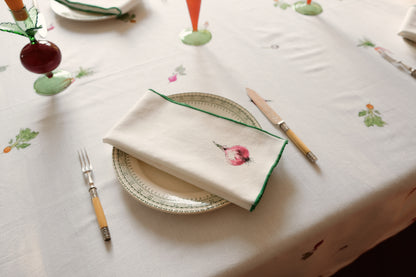Onion print napkin with a green overlock hem folded on a plate on the Root Vegetable Tablecloth