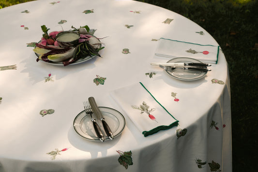 Spring Vegetable Tablecloth on a round table outdoors, set with radish print napkins, green-rimmed plates and a platter of spring vegetables
