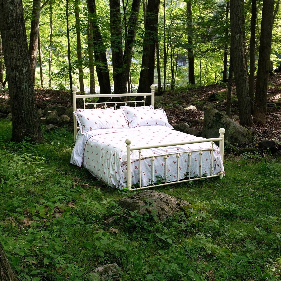 Crimson Meadows duvet set on a white iron bed in a green forest clearing