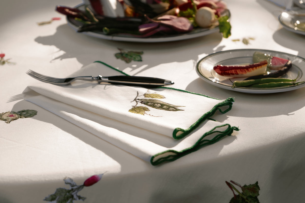 Peapod print napkin folded under a fork in dappled sunlight, showing the green overlock hem