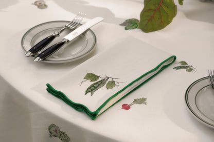 Peapod print napkin with a green overlock hem, folded beside a place setting
