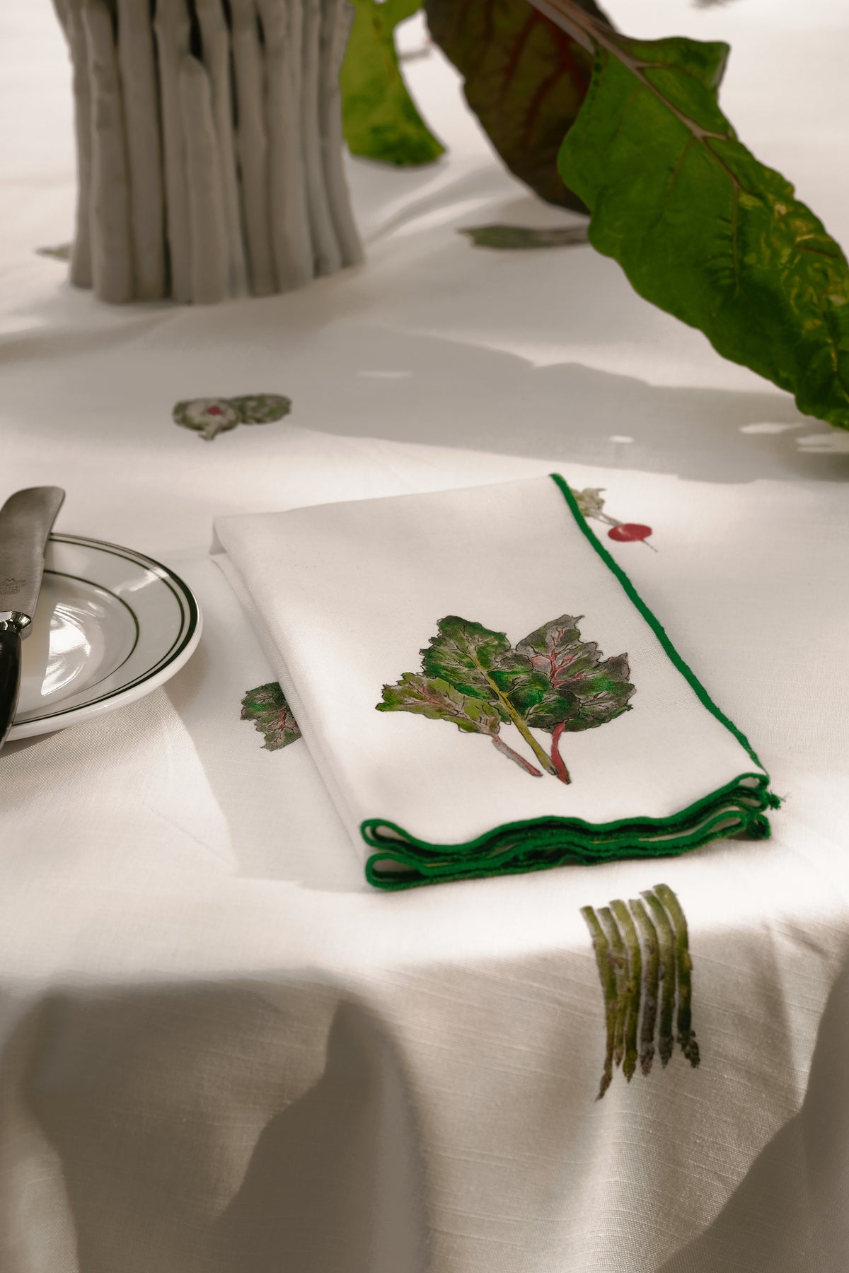 Swiss Chard print napkin with a green overlock hem, folded on a spring table setting