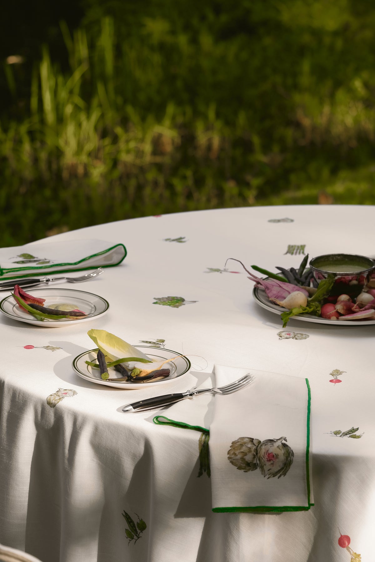 Spring table setting on the Spring Vegetable Tablecloth, with an artichoke print napkin and plates of fresh vegetables