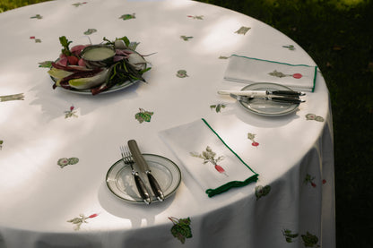 Spring Vegetable Tablecloth on a round table outdoors, set with radish print napkins, green-rimmed plates and a platter of spring vegetables