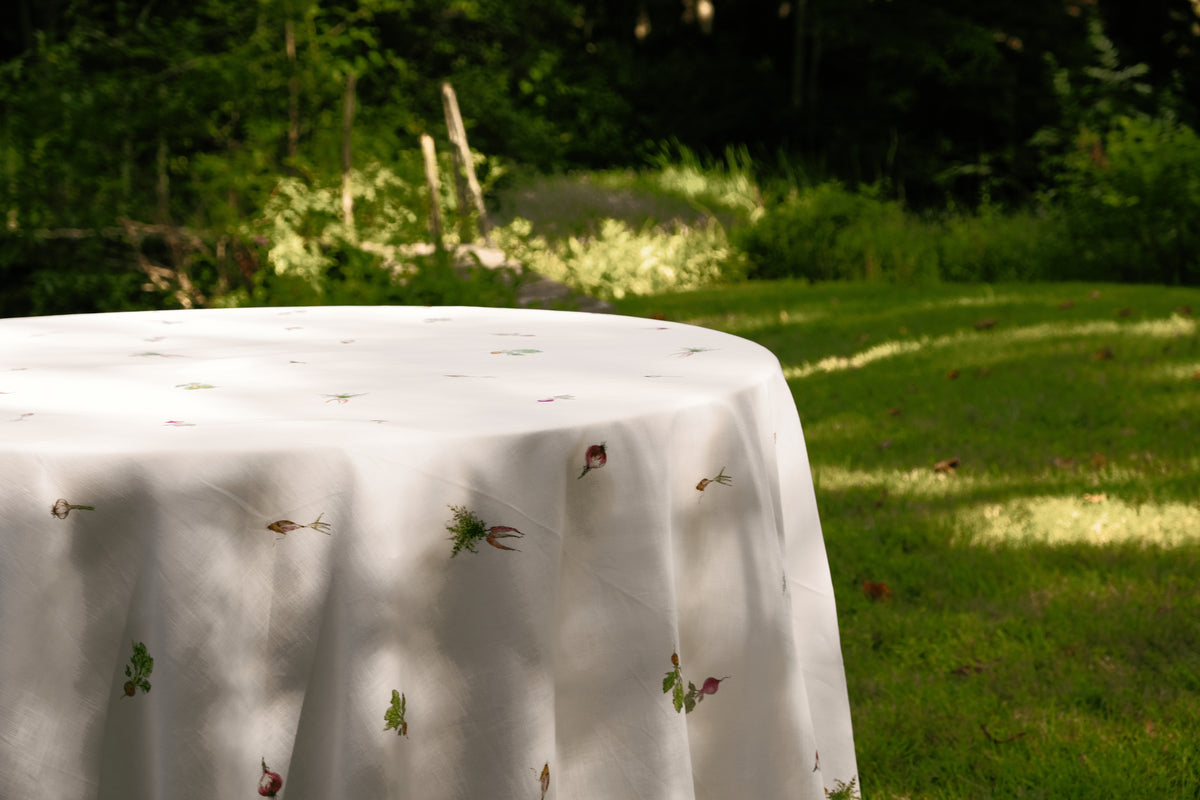 Spring Vegetable Tablecloth draped over a round table on a sunlit lawn, with vegetable motifs scattered across the cloth