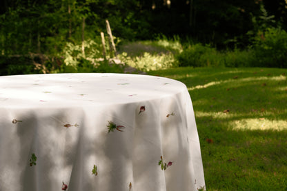 Spring Vegetable Tablecloth draped over a round table on a sunlit lawn, with vegetable motifs scattered across the cloth