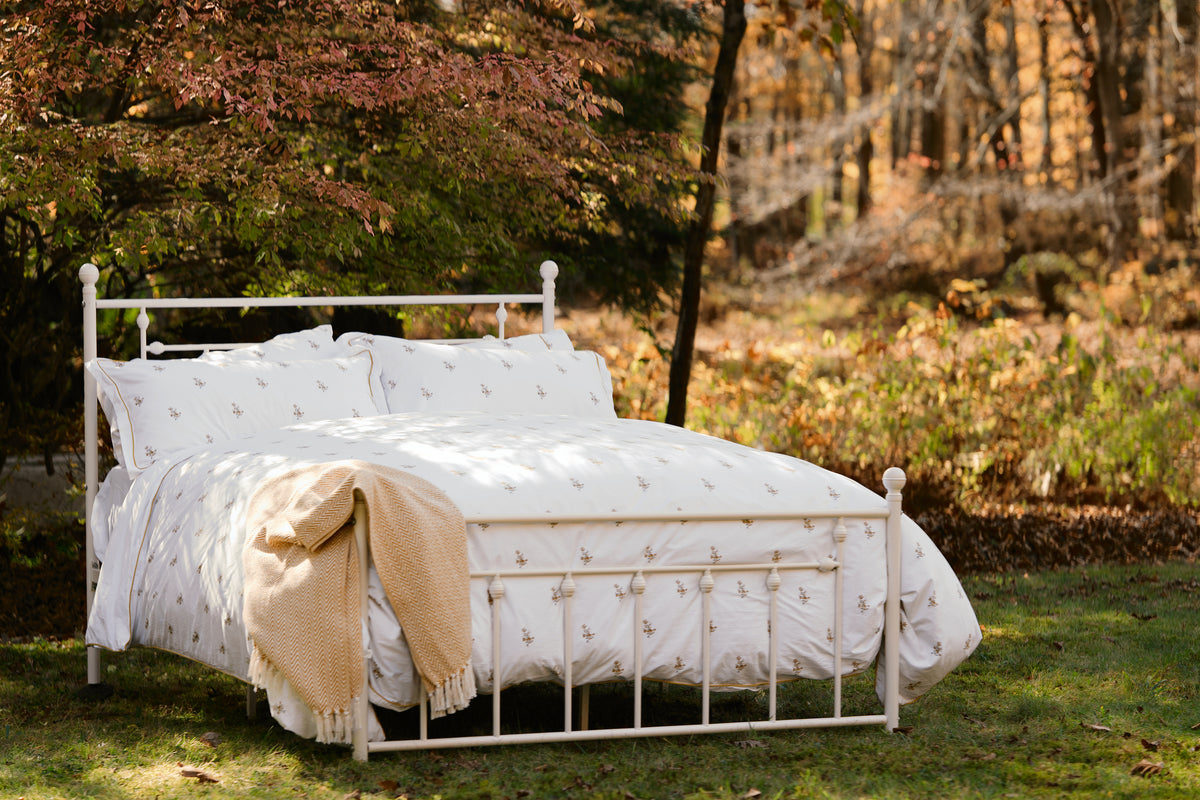 Fields of Gold bedding on a white iron bed outdoors in autumn, with a golden throw